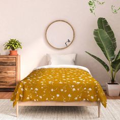 a bed in a bedroom with a yellow comforter and potted plant next to it