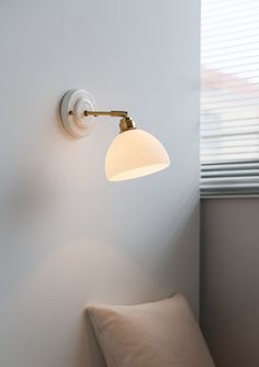 a white wall light mounted on the side of a wall next to a pillow and window