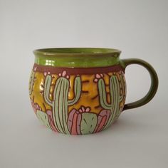 a green and yellow ceramic mug with cactus designs on the outside, sitting on a white surface