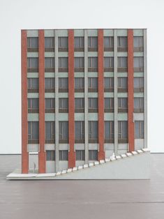 an architectural model of a building with red and grey stripes on the side, in front of a white wall