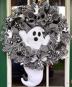 a wreath decorated with black and white striped ribbons, a ghost face on the front door