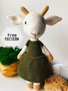 a crocheted sheep in a green dress next to some yarn and a plant