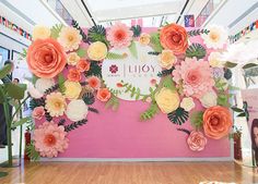 a pink and yellow flower display in a mall with people looking at the flowers on the wall