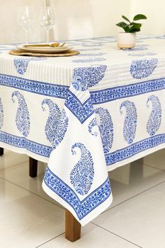 a blue and white table cloth on top of a wooden table with wine glasses in the background