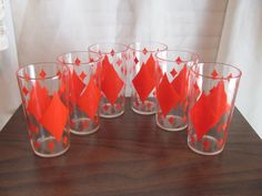 six red and silver glasses sitting on top of a wooden table