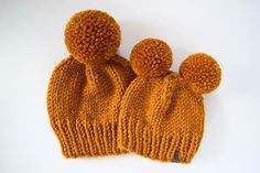 two orange knitted hats with pom - poms sitting on top of each other