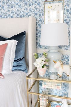 a white bed sitting next to a blue wall with flowers on it and a lamp