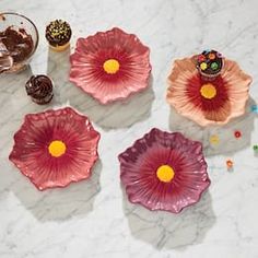 three pink flower shaped plates sitting on top of a marble table next to cupcakes