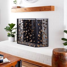 a clock mounted to the side of a white brick wall next to a table with plants