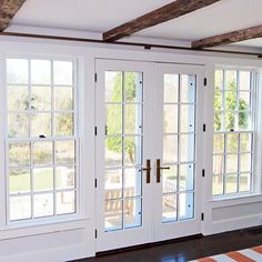 two white french doors are open on the inside of a room with wood floors and striped rug