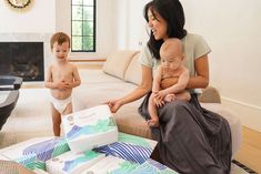 a woman sitting on a couch holding a baby in her lap and two other people standing around