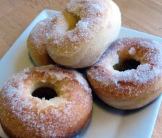 four donuts on a white plate covered in powdered sugar