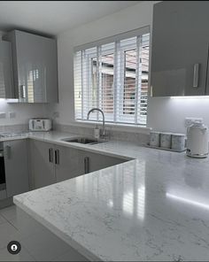 a kitchen with white marble counter tops and stainless steel appliances on the wall, along with large windows