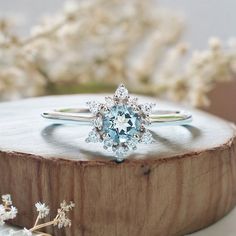 a blue and white diamond ring sitting on top of a piece of wood next to flowers