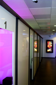 an empty hallway with glass partitions and purple lighting on the ceiling is pictured in this image