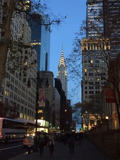 people are walking down the street in front of tall buildings at night with lights on