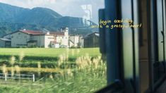 a view out the window of a train traveling past a green field with houses and mountains in the background