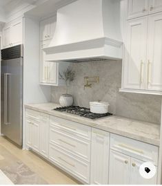 a kitchen with white cabinets and marble counter tops is shown in this image, there are two vases on the stove