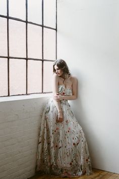 a woman in a dress leaning against a wall with her hand on her hip and looking out the window