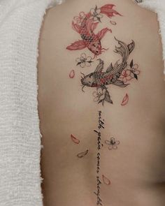 the back of a woman's body with flowers and fish tattoos on her ribs