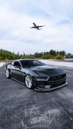 a large jetliner flying over a black sports car