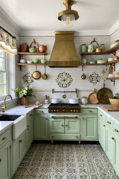 a kitchen with green cabinets and gold hood over the stove, pot racks on the wall