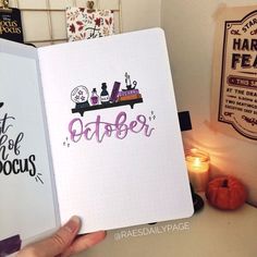 someone holding up a notebook with the word october written on it in front of some candles