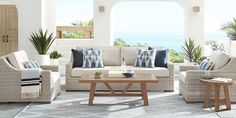 a living room filled with furniture next to an ocean view window and potted plants