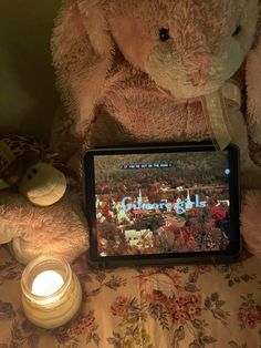 a teddy bear sitting on top of a bed next to a lit candle and tablet