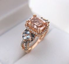 an engagement ring with two diamonds and a fancy pink morganite in the center on a white box