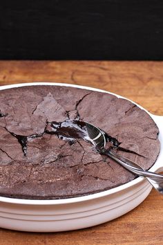 a white bowl filled with chocolate cake on top of a wooden table next to a fork