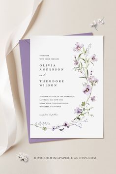 an elegant wedding card with purple flowers and greenery on the front is displayed next to a white ribbon