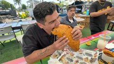 a man is eating food at an outdoor table with other people in the back ground