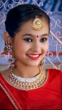 a woman in red is smiling and wearing gold jewelry on her head with an intricate design