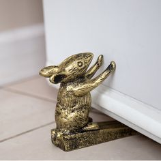 a gold rabbit figurine sitting on top of a white tile floor next to a wall