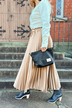 a woman in a skirt and sweater carrying a black bag on the steps with her handbag