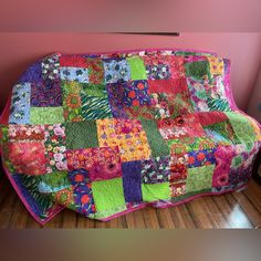 a couch covered in colorful patchwork on top of a hard wood floor next to a pink wall