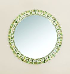 a round mirror with green and white tiles on the bottom is hanging on a wall