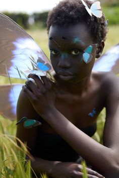 a woman with butterflies painted on her face sitting in the grass and holding a butterfly