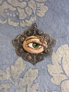 "Hand-painted Lover's Eye vintage silver filigree pendant. This piece of jewelry is a one of a kind, hand-painted by me on a vintage piece of jewelry selected also by me. It's painted with acrylic paint and varnished for protection and signed on the inside of the pin. The pendant is 1 3/4 wide x 1 1/2 inch wide. It comes with a silver plated chain - 18 inches long. \"The lover's eye is an 18th century variation on a portrait miniature of a secret love which typically displayed only the eye and e Vintage Hand Painted Round Pendant Necklace, Vintage Hand Painted Pendant Jewelry, Vintage Enamel Jewelry Handmade, Vintage Handmade Enamel Jewelry, Handmade Vintage Enamel Jewelry, Vintage Hand-painted Pendant Necklace, Vintage Hand Painted Pendant Necklace, Vintage Hand Painted Jewelry Gift, Vintage Hand Painted Jewelry For Gift