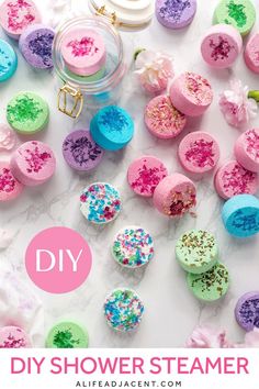 Dozens of shower steamers with various colours and decorations scene from above on a white marble background. Text overlay: DIY shower steamer. Make Shower Steamers, Shower Fizzies, Shower Melts, Shower Tablets, Shower Aromatherapy, Diy Spa Day, Steamer Recipes