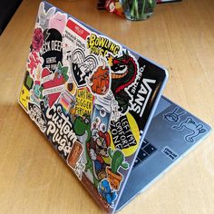 a laptop covered in stickers sitting on top of a wooden table next to a plant