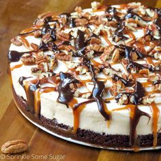 a cheesecake with nuts and caramel drizzle on top is sitting on a wooden table