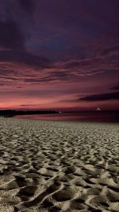 the sky is purple and pink as the sun sets on the beach with waves in the sand