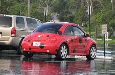 a small red car is parked in the rain next to a silver van that has been painted with black spots