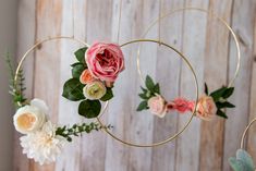 three flowers are hanging from a gold hoop with greenery on the bottom and one flower is pink, white and yellow