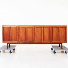 a wooden cabinet sitting on wheels in front of a white wall with two blue wheels next to it