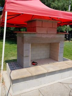 DIY Outdoor Fireplace built from cinderblock and mortar. Concrete and steel inside with firebrick. Red tent over the fireplace for sun and weather protection. Flagstone seating hearth. Green trees and grass in background. Yard Fireplace Ideas, Diy Outdoor Fireplace Easy Brick, Diy Brick Outdoor Fireplace, Fireplace Outside Fire Pits, Cinderblock Fireplace Outdoor, Diy Outside Fireplace How To Build, Cinder Block Fireplace Diy, Cinderblock Fireplace Diy, Small Backyard Fireplace Ideas