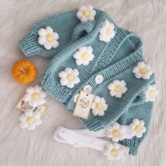 a knitted sweater and hat with flowers on the front, sitting on a white furnishing