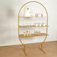 a gold shelf with cupcakes and cakes on it in front of a white wall